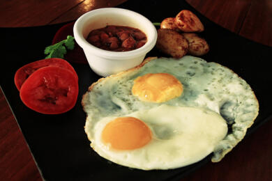 Two sunnyside up eggs with side of beans on black plate