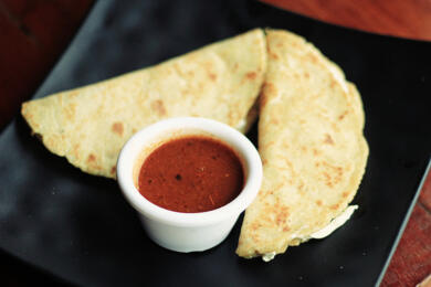 Two cheese quesadillas with red sauce on black plate